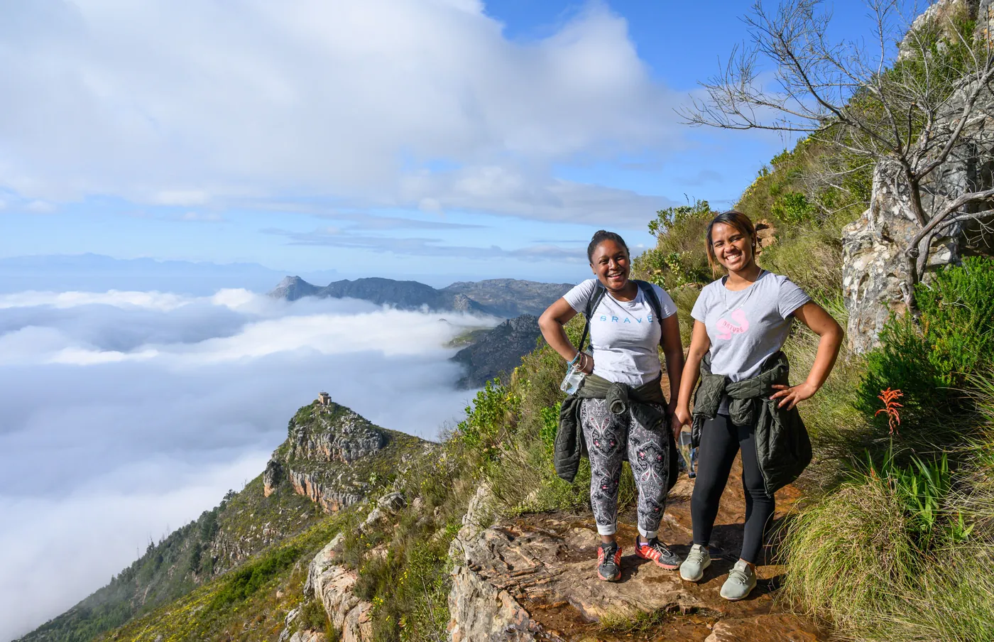 Two young women from BRAVE on a mountain trail above the clouds